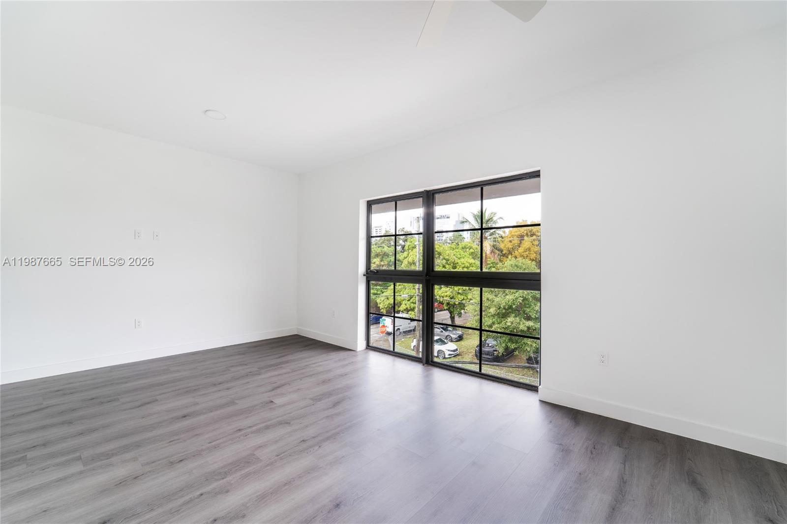 An empty room features white walls, dark wood-look flooring, and large black-framed windows — 1165 NW 8th Ave # 101, Miami FL 33136, MIAMI, FL