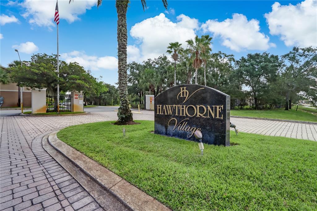 A stone monument sign for Hawthorne Village stands on a grassy island near a driveway — 9942 TURF WAY UNIT 1, ORLANDO, FL