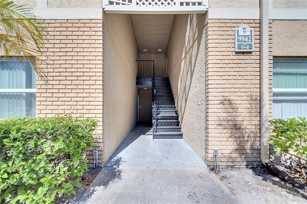 An exterior view of a building entrance with a concrete walkway and a staircase — 9942 TURF WAY UNIT 1, ORLANDO, FL