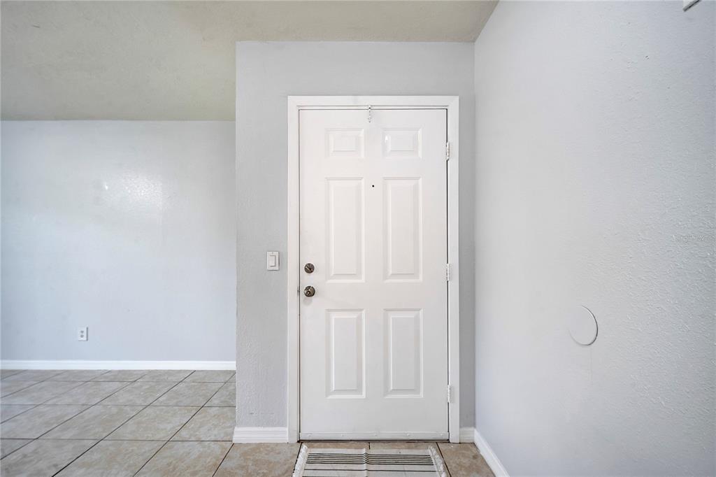 A white front door with a peephole is centered in a room with tiled floors — 9942 TURF WAY UNIT 1, ORLANDO, FL