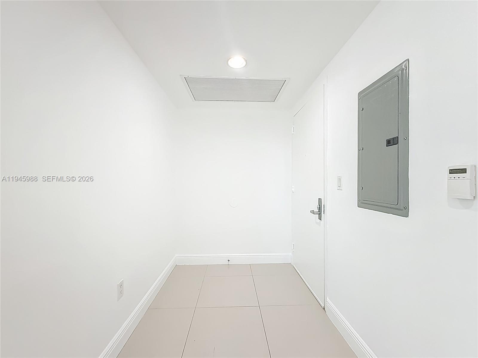 A minimalist hallway features white walls, light-colored floor tiles, a recessed light, and an electrical panel — 475 Brickell Ave # 4215, Miami FL 33131, MIAMI, FL