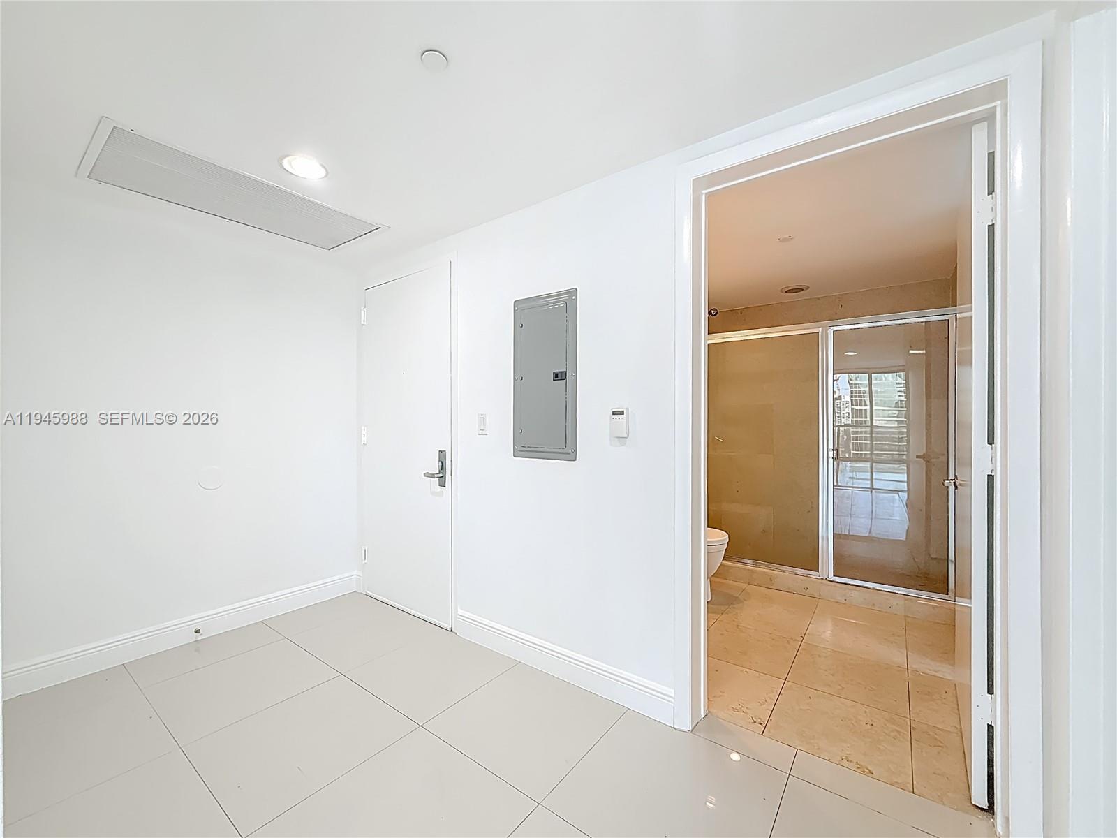 A white-walled room with tile flooring, a circuit breaker panel, and an open bathroom doorway — 475 Brickell Ave # 4215, Miami FL 33131, MIAMI, FL