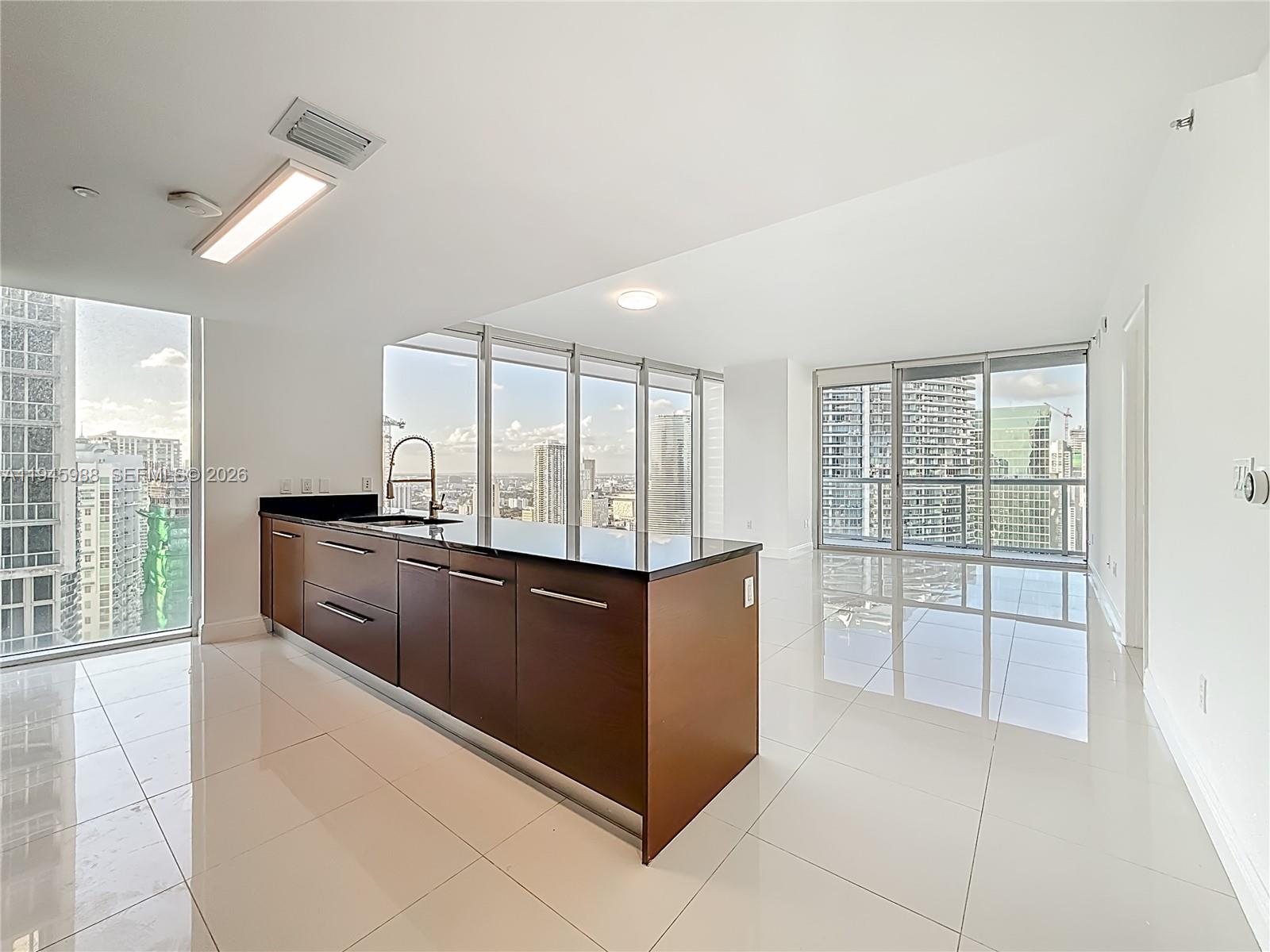 A modern kitchen island with dark cabinetry and black countertops sits in a bright apartment — 475 Brickell Ave # 4215, Miami FL 33131, MIAMI, FL