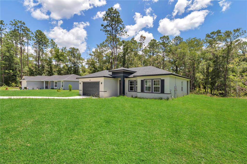 A modern single-story house with a dark garage and gray trim sits on a grassy lot — 219 E CALDWELL DRIVE, DUNNELLON, FL