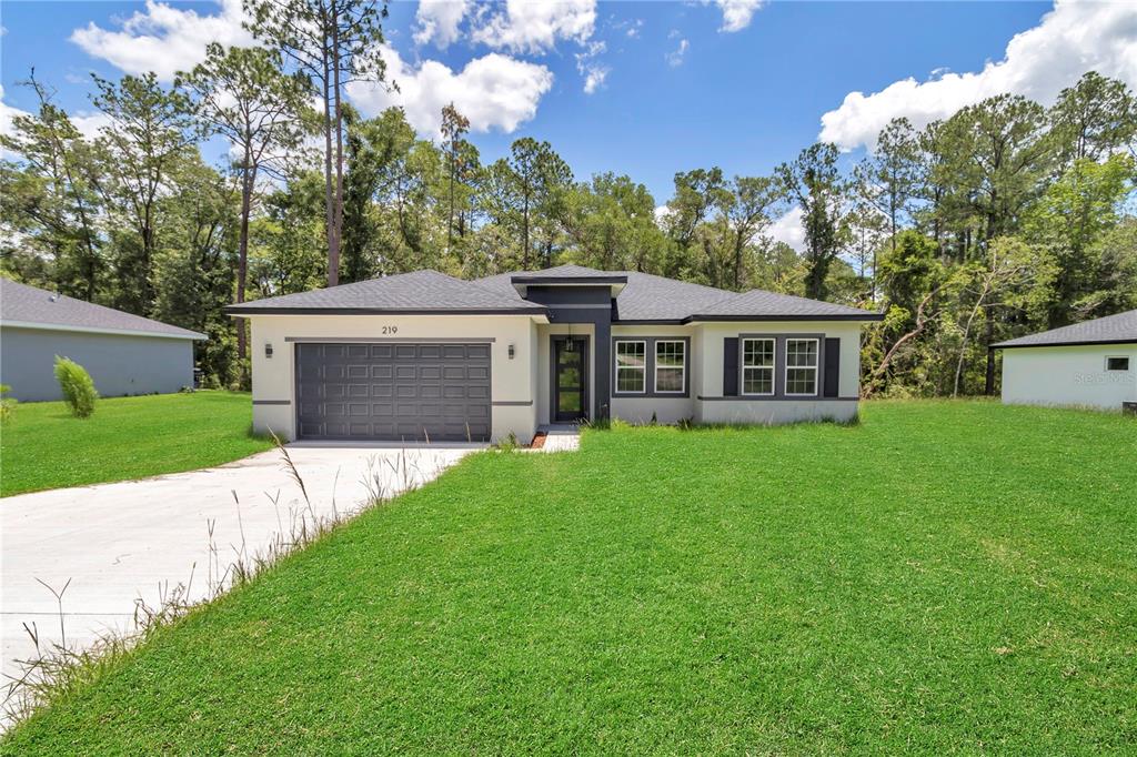 A single-story house with a gray garage, dark trim, and a lawn under a blue sky — 219 E CALDWELL DRIVE, DUNNELLON, FL
