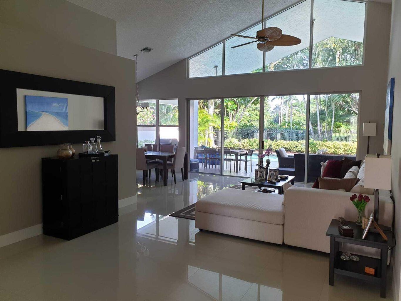 A living room with vaulted ceilings, tile floors, and large windows overlooking a patio area — 5463 NW 20th Avenue, Boca Raton FL 33496, BOCA RATON, FL