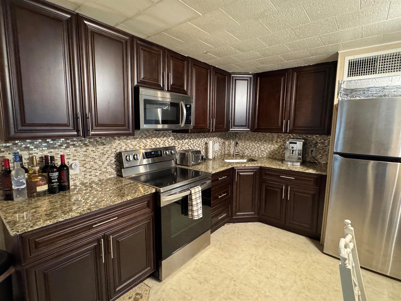 A kitchen features dark wood cabinets, stainless steel appliances, granite countertops, and a tiled backsplash — 8926 Palm Street, Boynton Beach FL 33436, BOYNTON BEACH, FL