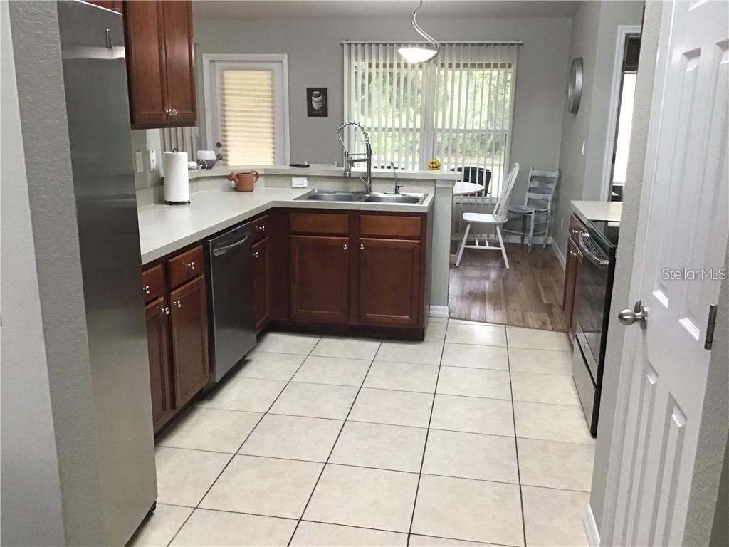 A kitchen with wood cabinets, stainless steel appliances, and tile flooring overlooks a dining area — 2091 SNOWFLAKE LANE, NORTH PORT, FL