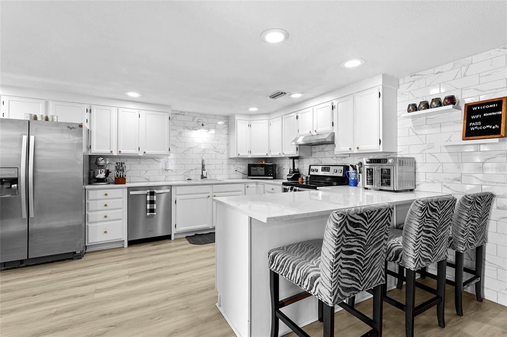 A white kitchen features light wood-look flooring, stainless steel appliances, and a breakfast bar — 831 WINTER GARDEN DRIVE, SARASOTA, FL