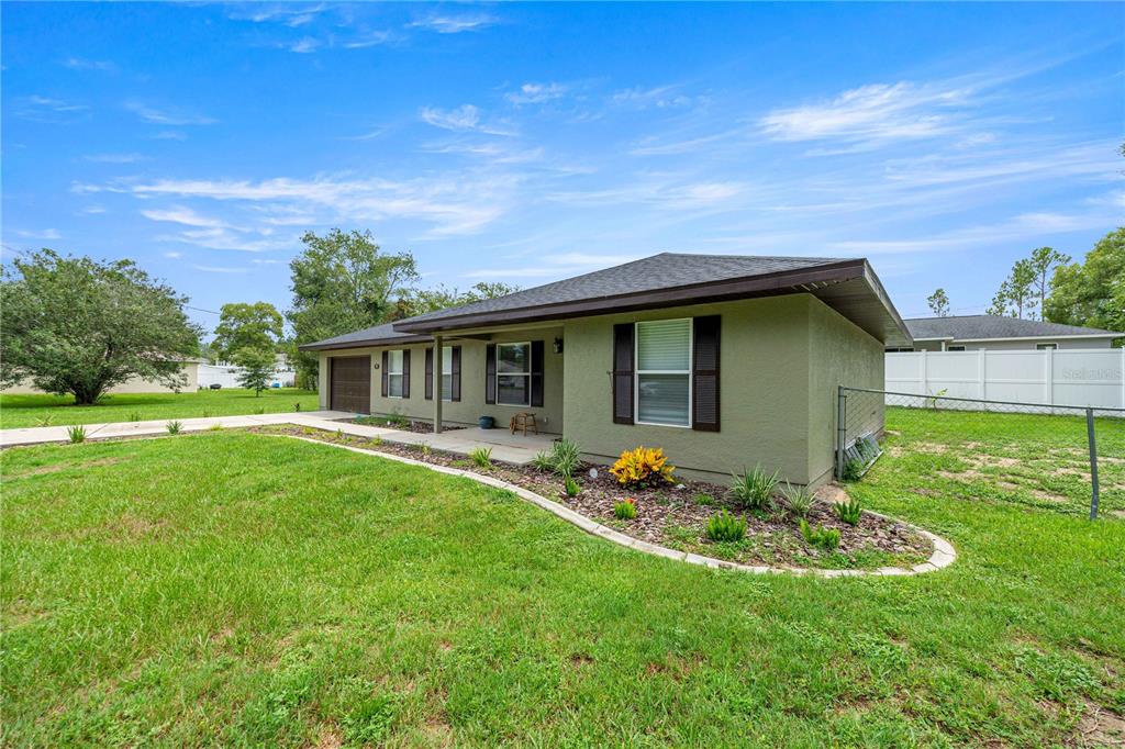 A single-story house with green stucco siding, a dark roof, and a landscaped front garden — 80 PECAN RUN COURSE, OCALA, FL