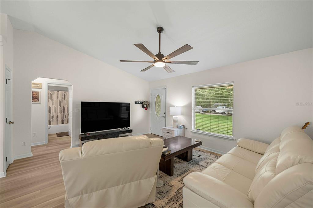 A living room features a light-colored sofa, a television, a ceiling fan, and wood flooring — 80 PECAN RUN COURSE, OCALA, FL