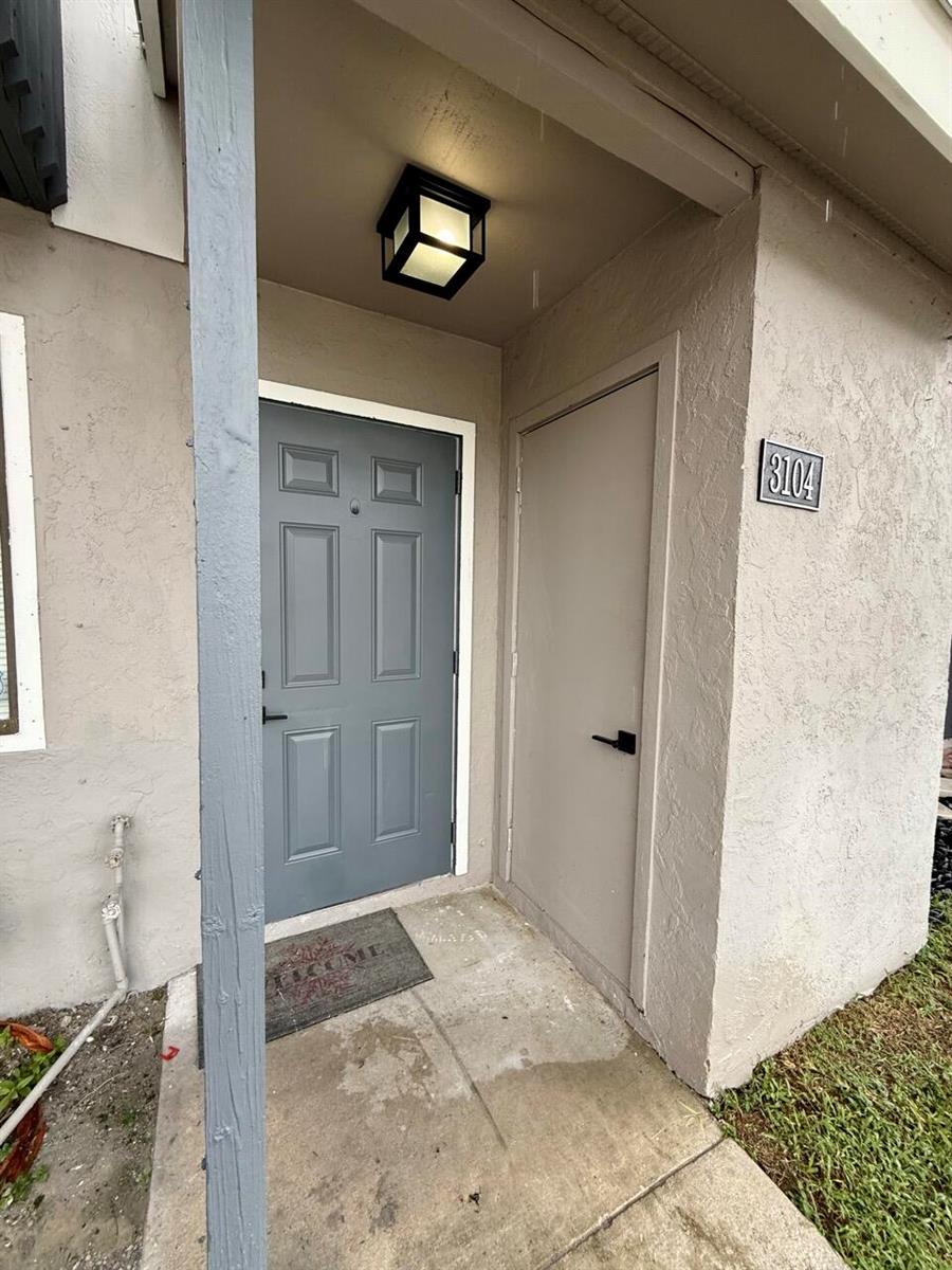 The exterior entrance features a gray front door, a utility closet, and a porch light — 3104 Poolside Drive, FL 33463, FL