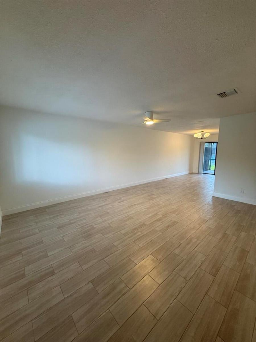 An empty living room features light wood-look tile flooring, white walls, and a ceiling fan — 3104 Poolside Drive, FL 33463, FL