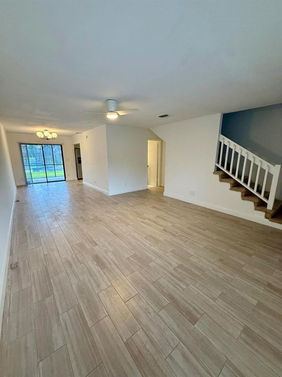 An open living area features wood-look tile flooring, a ceiling fan, and a staircase — 3104 Poolside Drive, FL 33463, FL