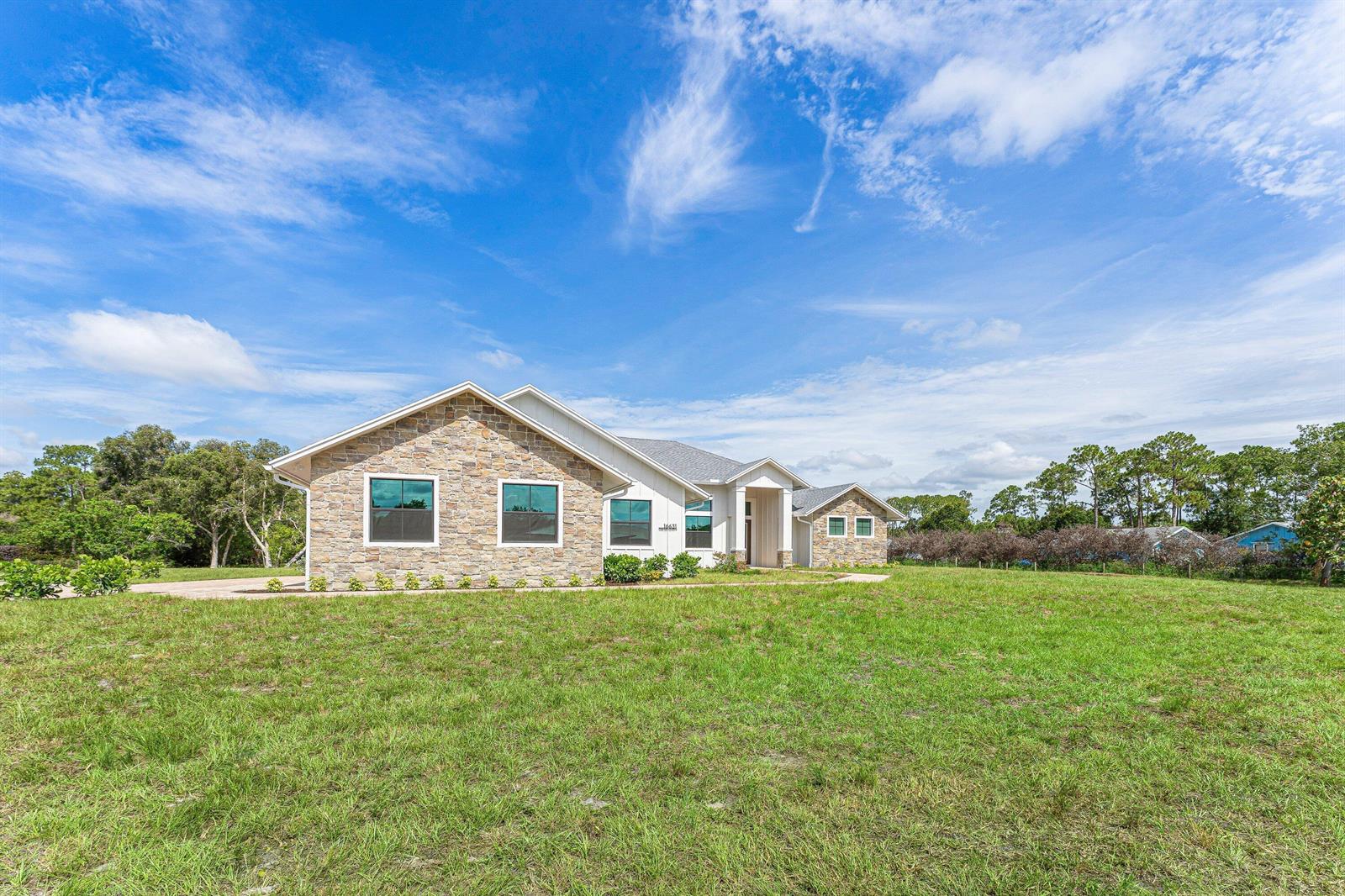A single-story house with a stone facade and a large grassy yard under a blue sky — 16631 132nd Terrace N, Jupiter FL 33478, JUPITER, FL