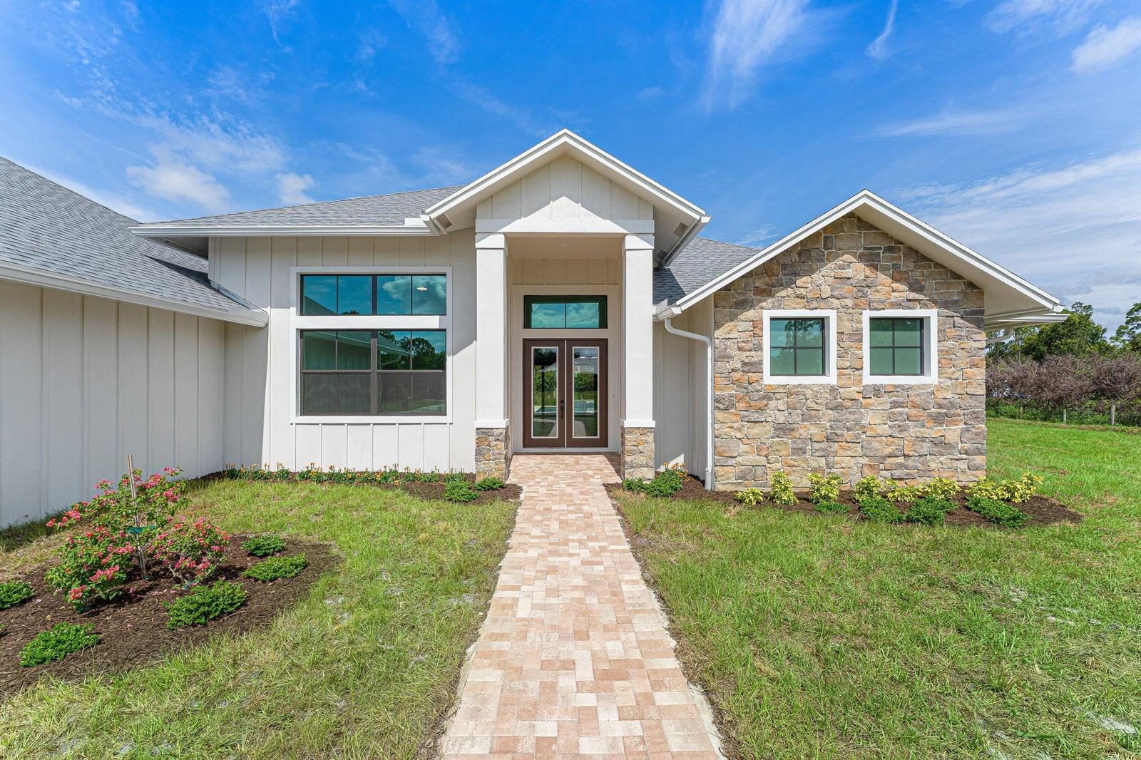 The exterior of a modern house features white vertical siding, stone veneer, and a walkway — 16631 132nd Terrace N, Jupiter FL 33478, JUPITER, FL