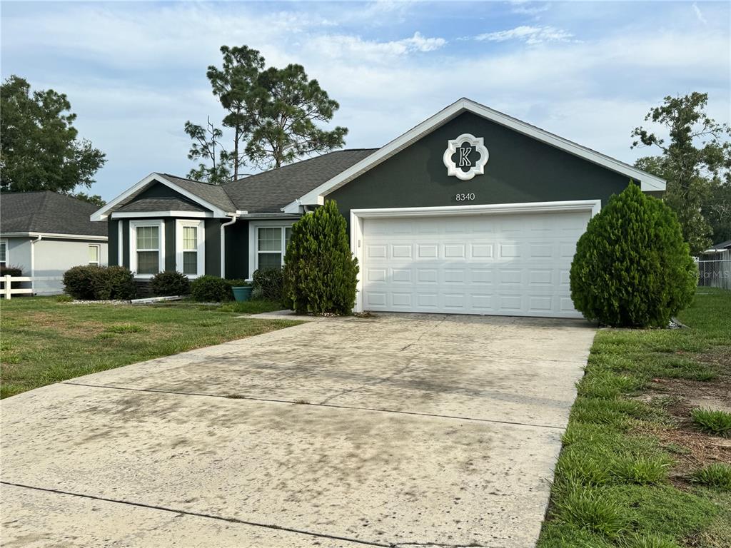 A dark green single-story house with a white garage door and a concrete driveway — 8340 SE 159TH LANE, SUMMERFIELD, FL