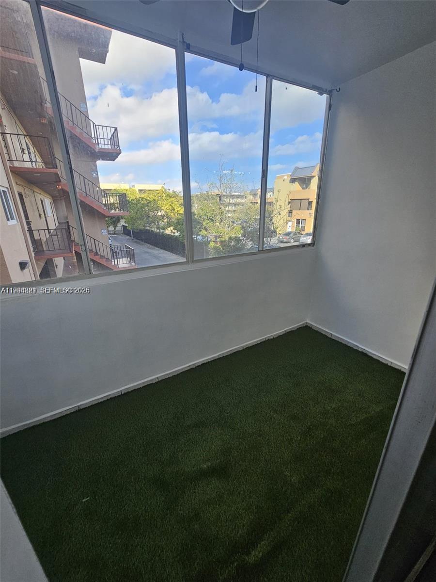 An enclosed balcony features white walls, a ceiling fan, and green artificial turf flooring — 6055 W 19th # 209, Hialeah FL 33012, HIALEAH, FL