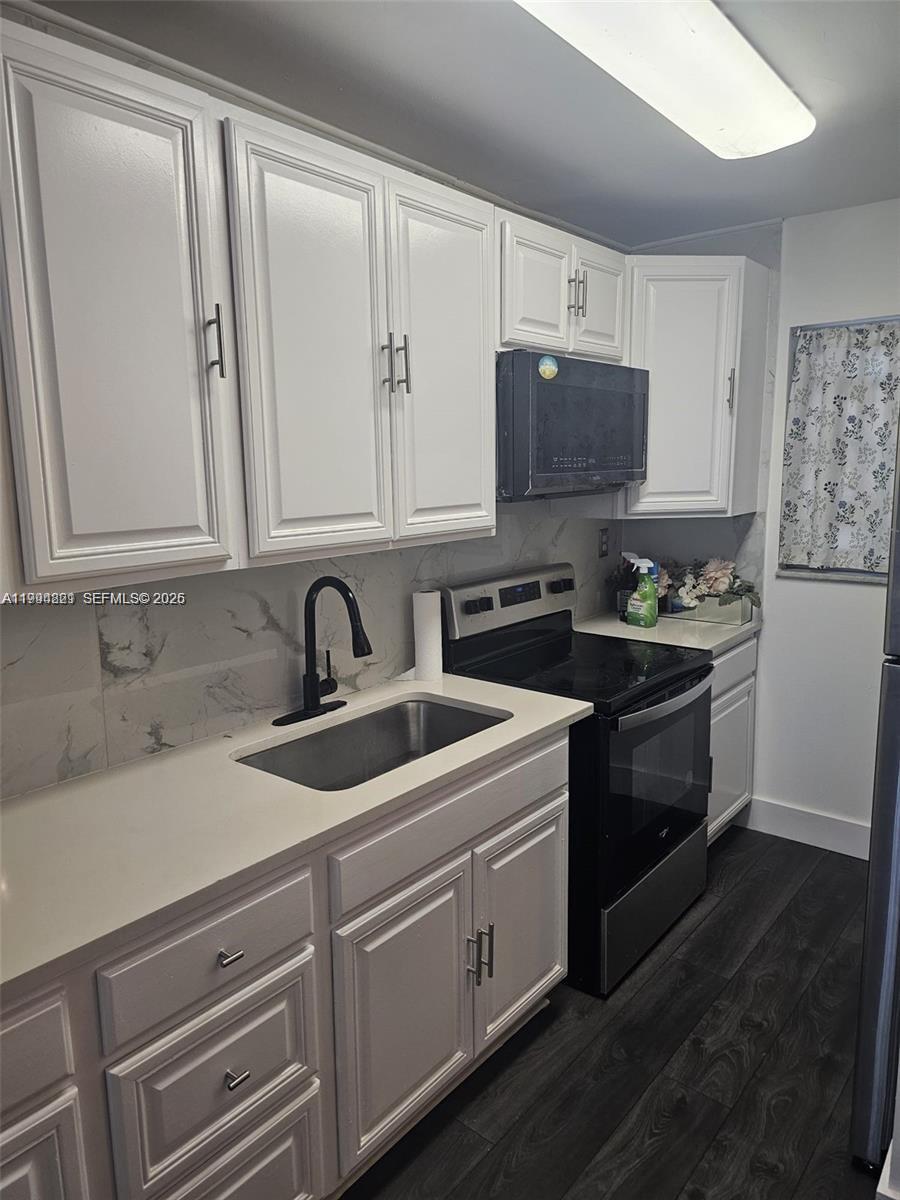 A kitchen features white cabinets, a black microwave, a black stove, and a stainless sink — 6055 W 19th # 209, Hialeah FL 33012, HIALEAH, FL