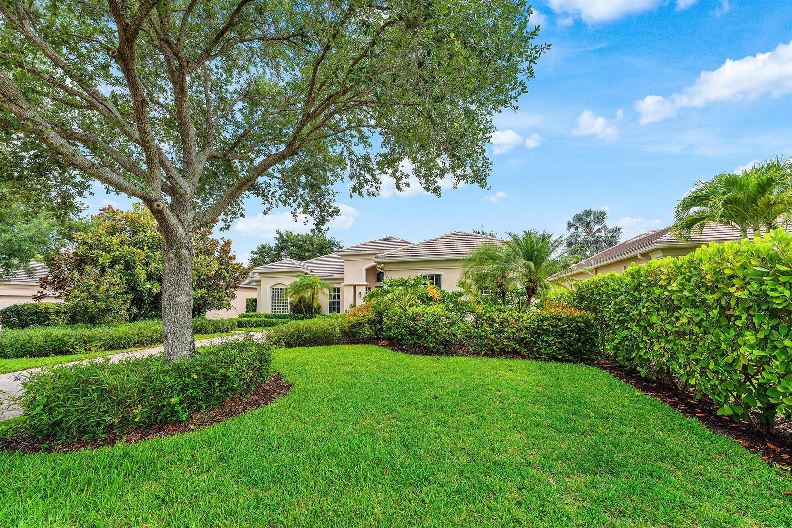 A single-story house with a tiled roof sits behind a manicured lawn and lush landscaping — 2068 Wightman Drive, Wellington FL 33414, WELLINGTON, FL