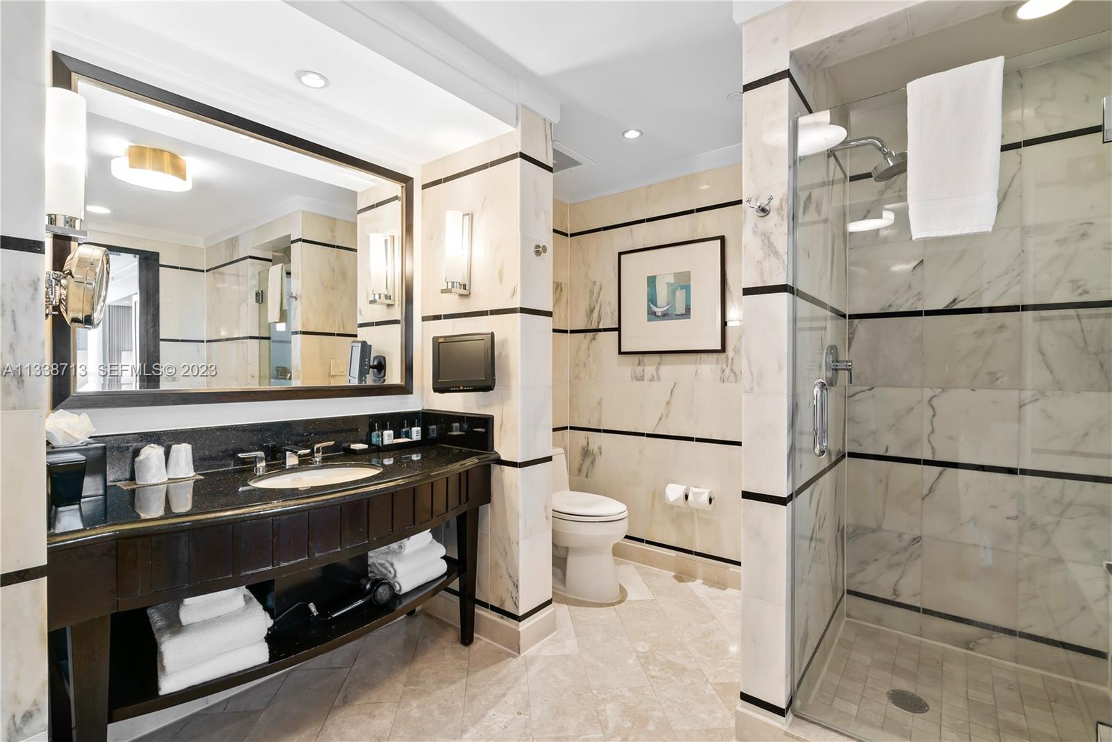 A bathroom features a black vanity, marble wall tiles with black accents, and a glass shower — 4391 Collins Ave, Miami Beach FL 33140, MIAMI BEACH, FL
