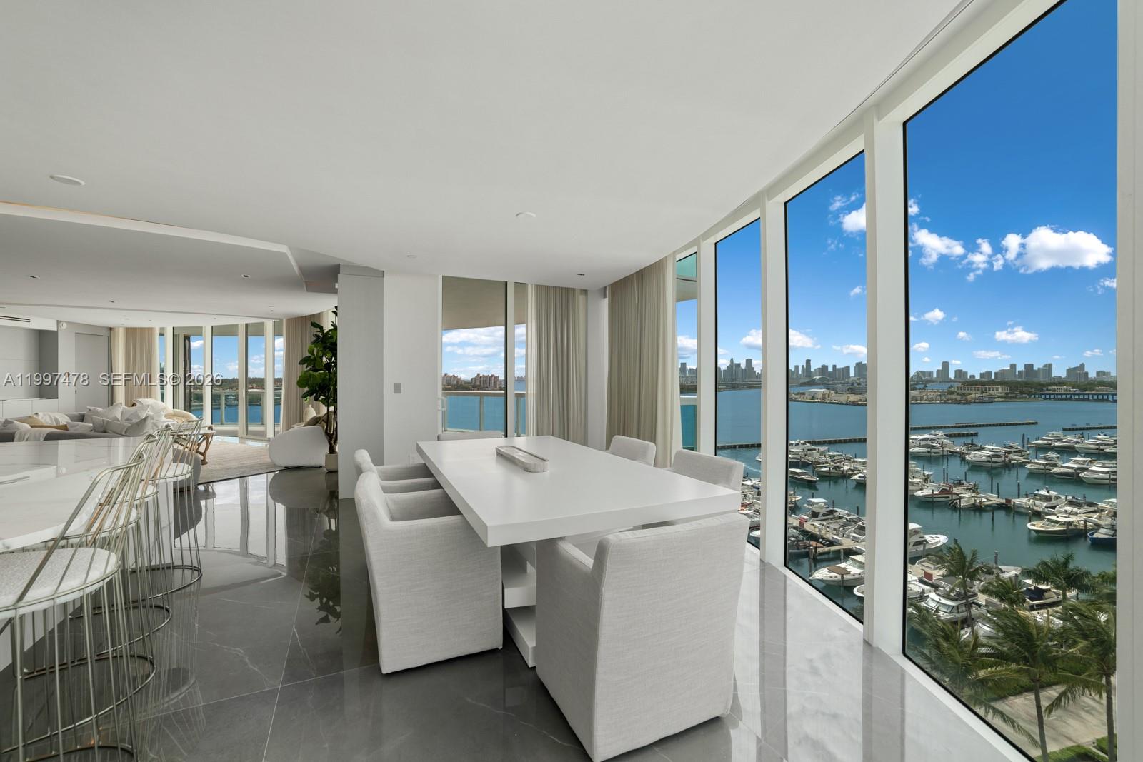 A modern dining area with a white table, upholstered chairs, and floor-to-ceiling harbor views — 1000 S Pointe Dr # 901, Miami Beach FL 33139, MIAMI BEACH, FL