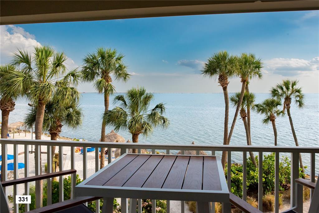 A balcony with a table overlooks a sandy beach, palm trees, and the ocean — 2506 N ROCKY POINT DRIVE UNIT 331 and #275, TAMPA, FL