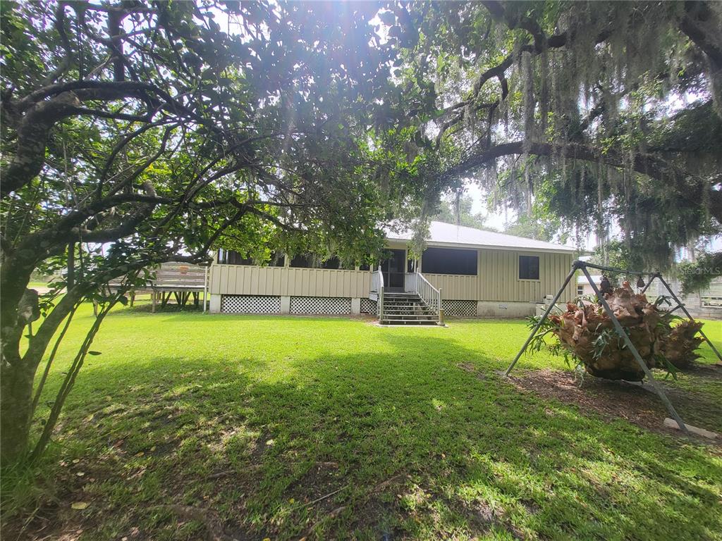 A tan house with a screened porch and stairs sits in a grassy yard with trees — 32531 4TH AVENUE, SAN ANTONIO, FL