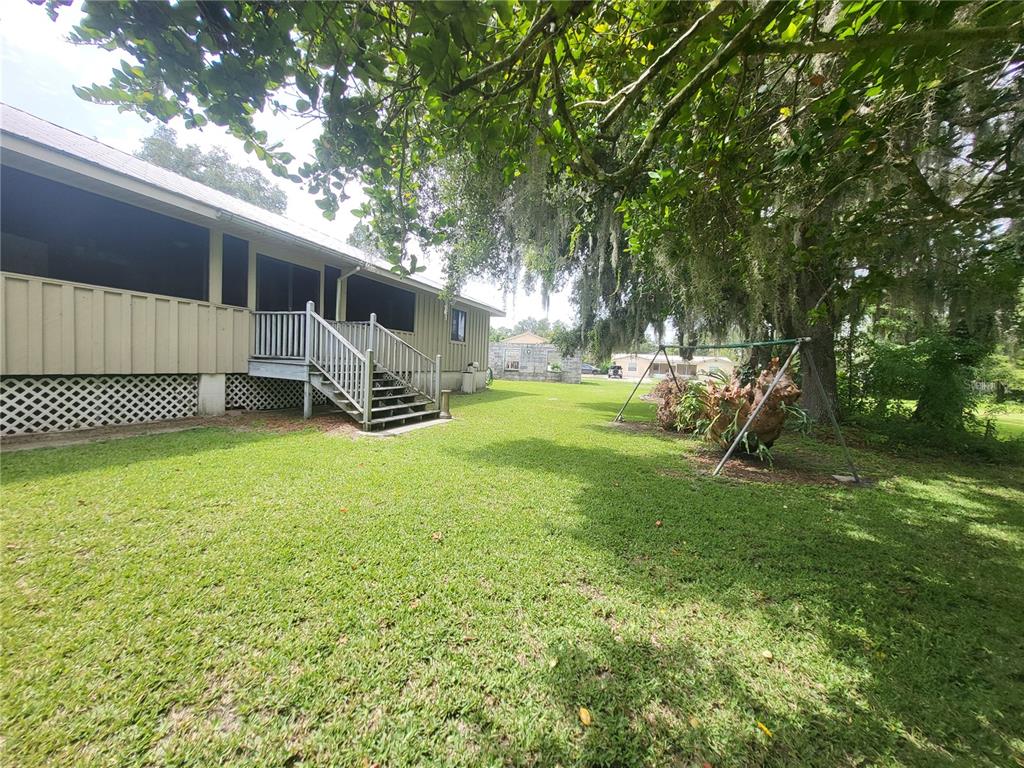 A grassy backyard features a house with a screened porch, wooden stairs, and a swing set — 32531 4TH AVENUE, SAN ANTONIO, FL