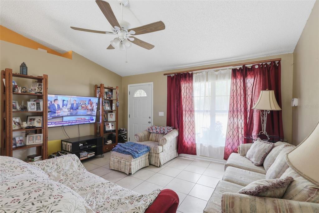 A living room features a ceiling fan, tiled floors, a television, and red window curtains — 1496 10TH STREET, ORANGE CITY, FL