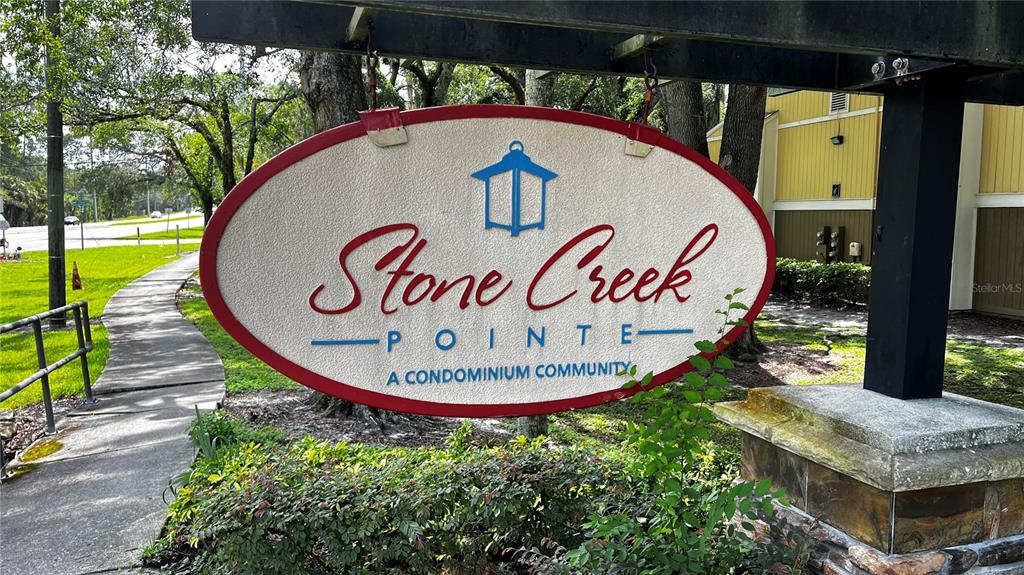 An oval sign for Stone Creek Pointe condominium community hangs from a wooden structure outdoors — 13289 ARBOR POINTE CIRCLE UNIT 202, TAMPA, FL