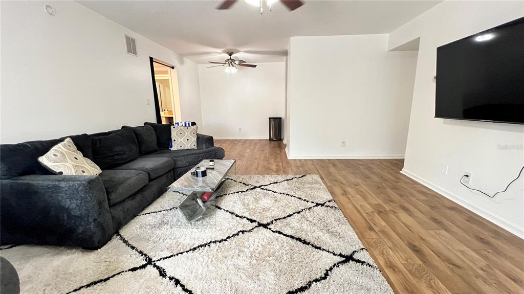 A living room features a dark sectional sofa, a glass coffee table, and wood flooring — 13289 ARBOR POINTE CIRCLE UNIT 202, TAMPA, FL