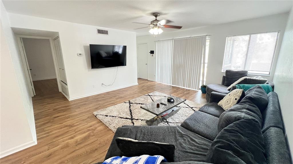 A living room features wood-look flooring, a gray sectional sofa, a television, and a rug — 13289 ARBOR POINTE CIRCLE UNIT 202, TAMPA, FL
