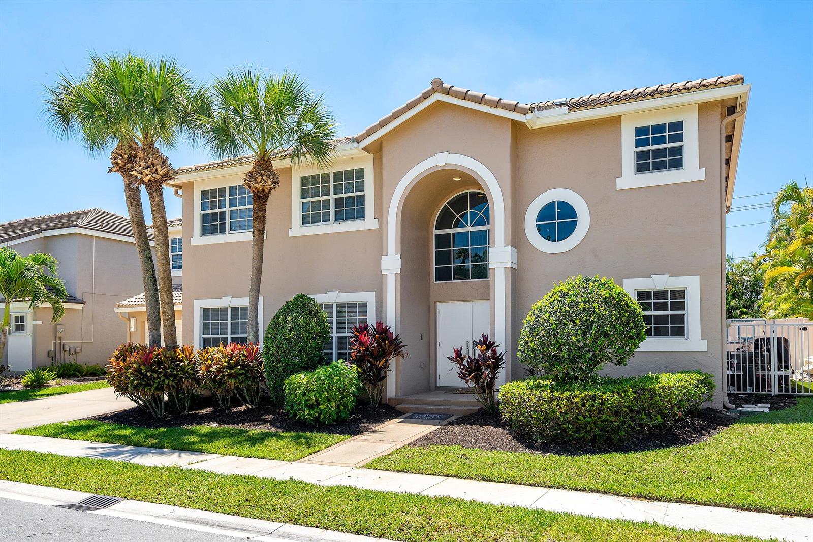 A two-story tan house with a tiled roof, arched entryway, and palm trees in front — 10616 Wheelhouse Circle, Boca Raton FL 33428, BOCA RATON, FL