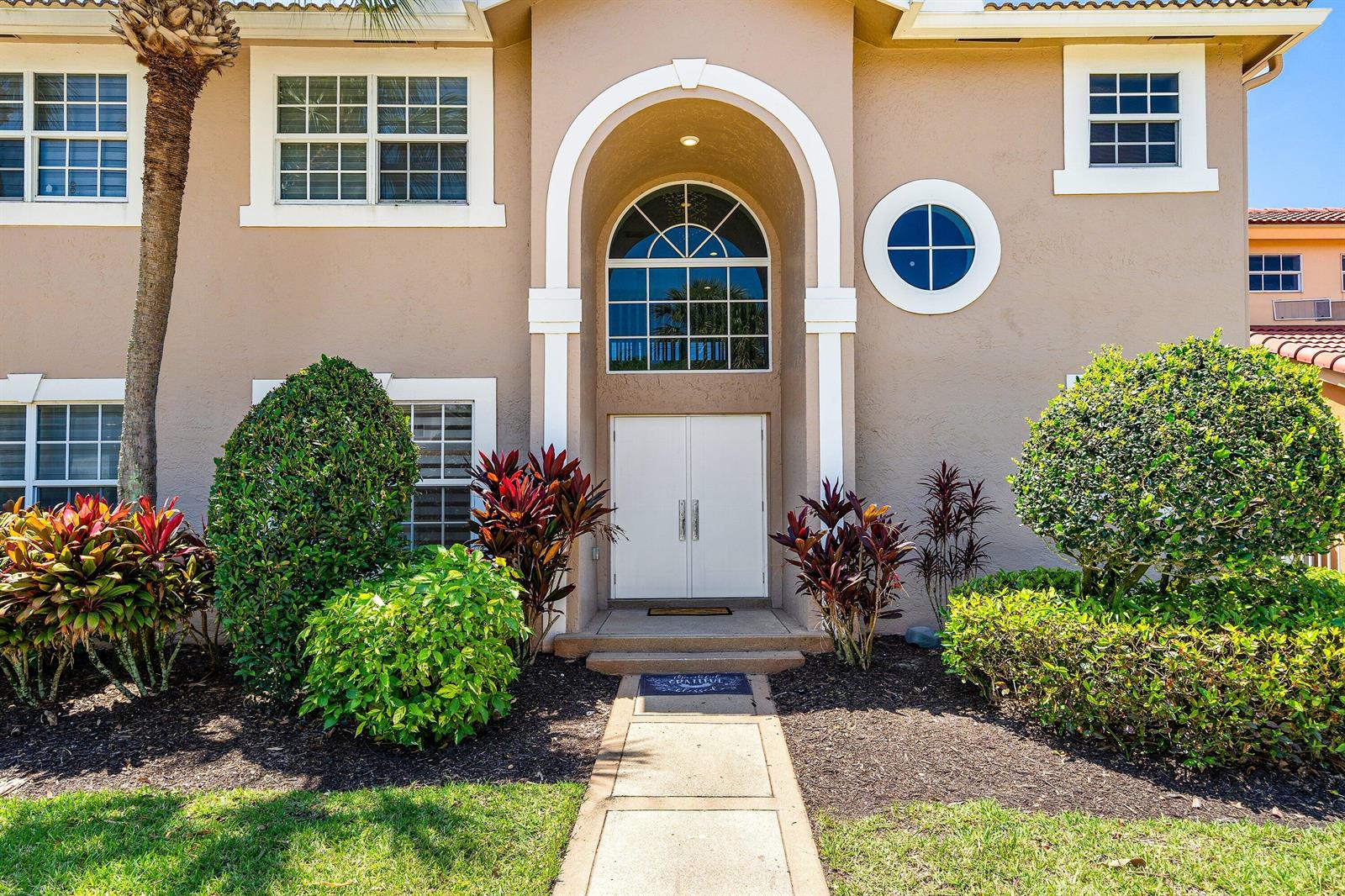 The exterior of a two-story beige house features a white arched entryway and double doors — 10616 Wheelhouse Circle, Boca Raton FL 33428, BOCA RATON, FL