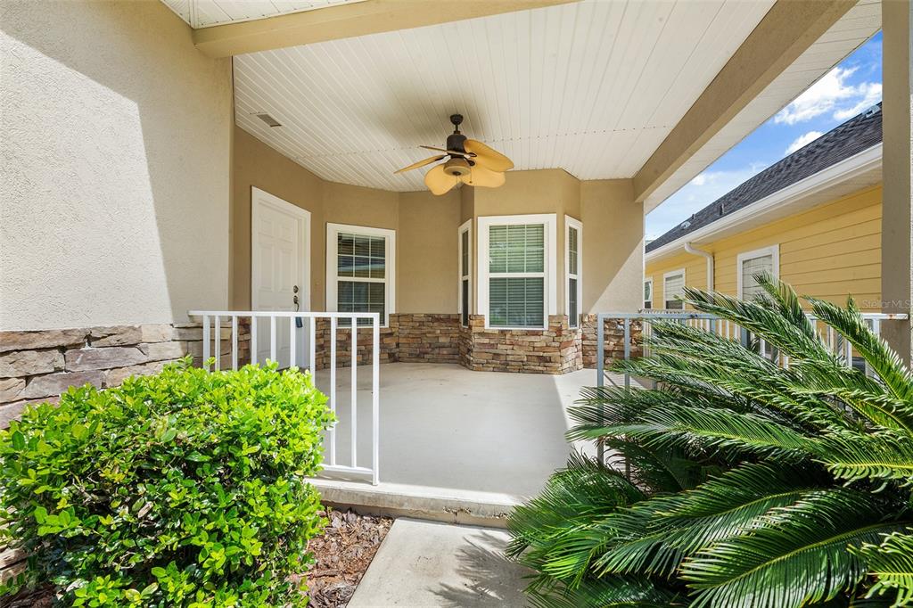 A covered porch features a ceiling fan, stone accents, and white railings — 1125 NW 120TH WAY, GAINESVILLE, FL