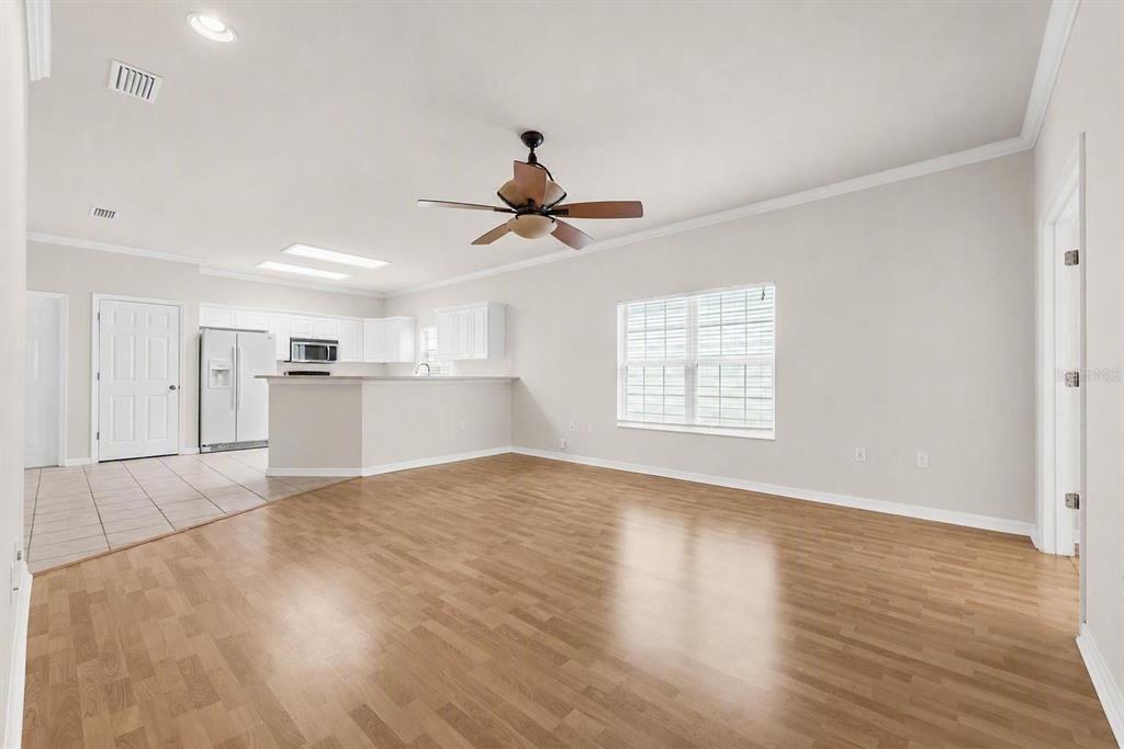 An open-concept living room with wood flooring, a ceiling fan, and an adjacent kitchen area — 1125 NW 120TH WAY, GAINESVILLE, FL