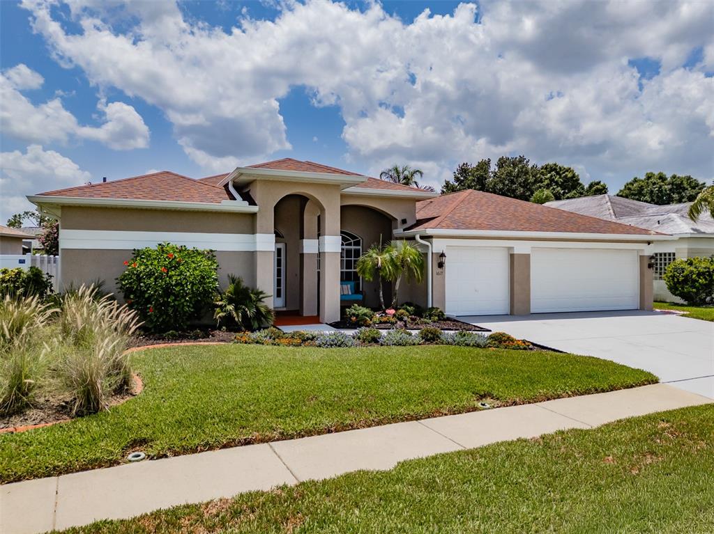 A single-story suburban house features a tan stucco exterior, a two-car garage, and landscaping — 1617 VISTOSO LANE, SUN CITY CENTER, FL