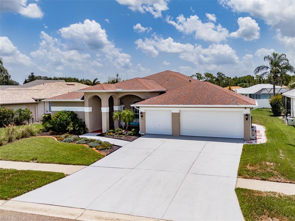 A single-story suburban house with a two-car garage, arched entryway, and a brown shingled roof — 1617 VISTOSO LANE, SUN CITY CENTER, FL