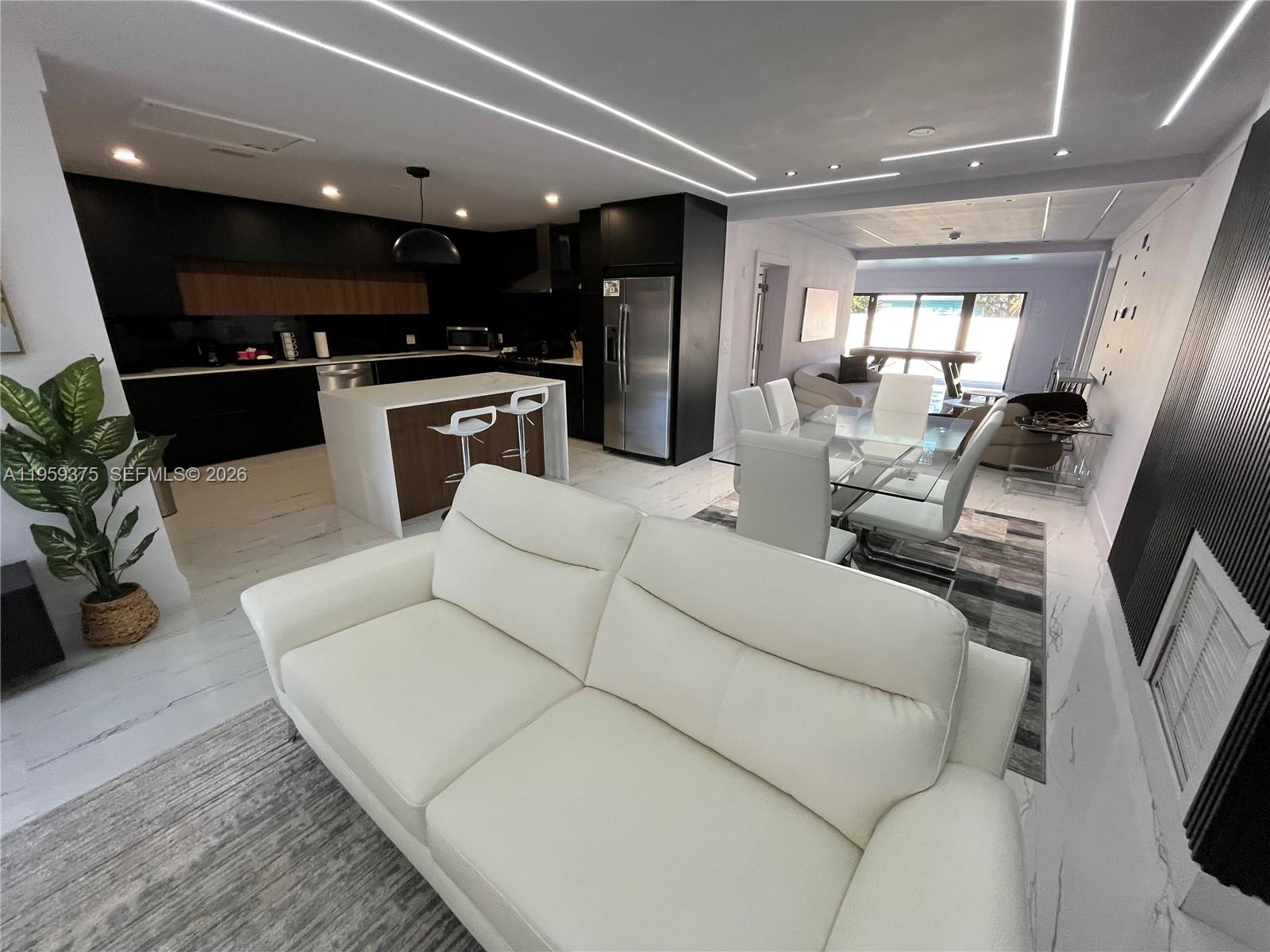 An open-concept living and dining area features a modern kitchen with dark cabinetry and island — 39 SE 7th St # 0, Dania Beach FL 33004, DANIA BEACH, FL