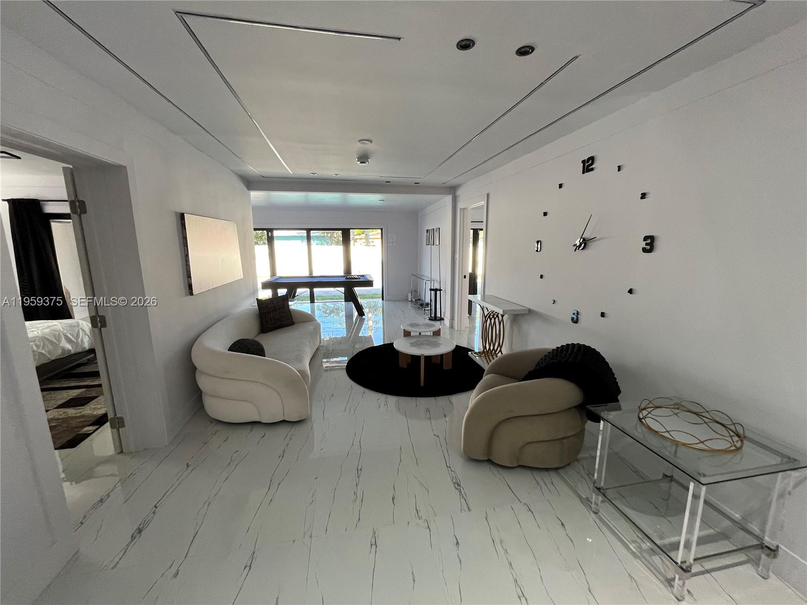 A modern living room features white marble floors, a large wall clock, and a pool table — 39 SE 7th St # 0, Dania Beach FL 33004, DANIA BEACH, FL