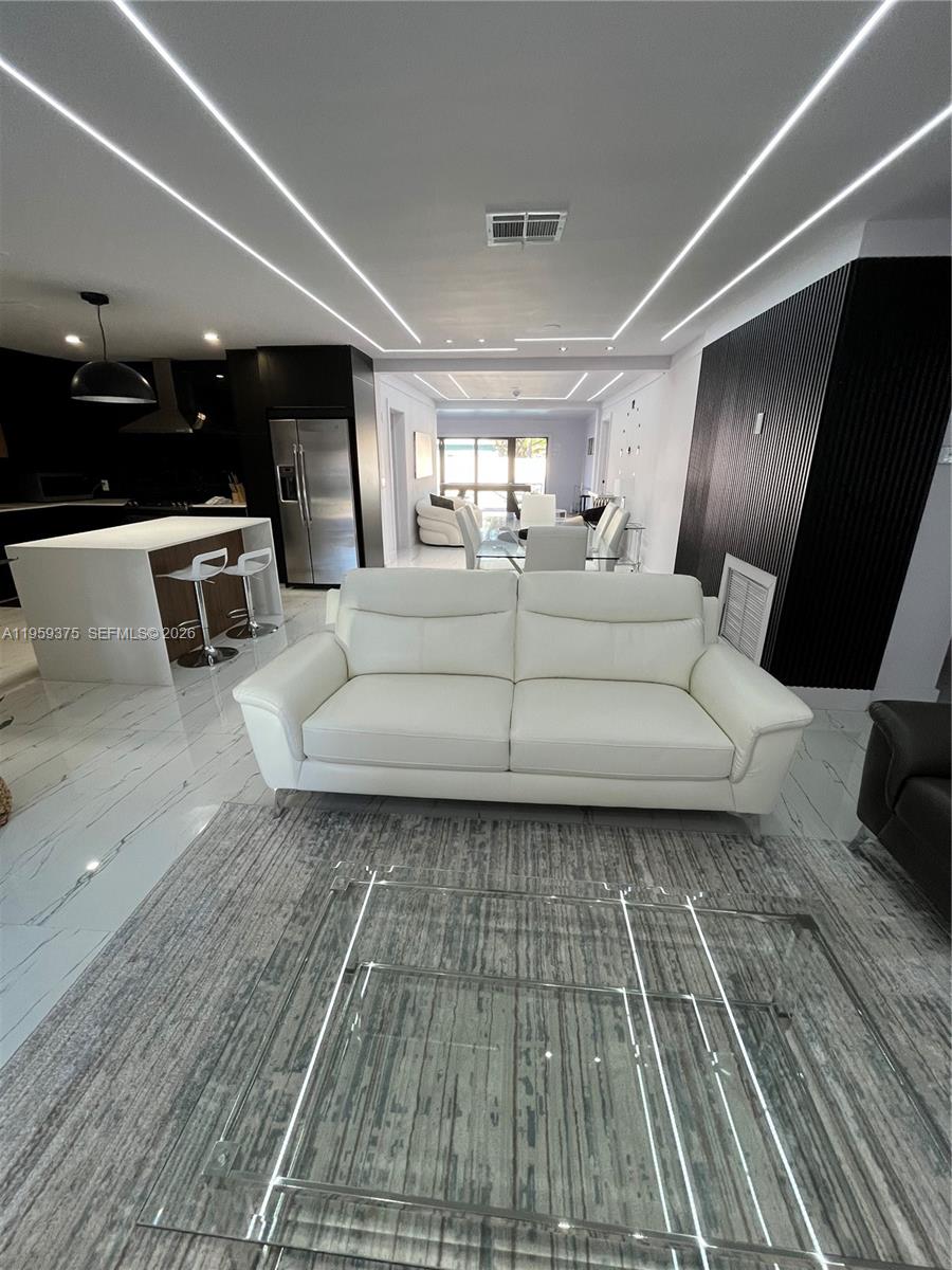 A modern open-concept living room and kitchen feature white leather furniture, tile flooring, and recessed lighting — 39 SE 7th St # 0, Dania Beach FL 33004, DANIA BEACH, FL