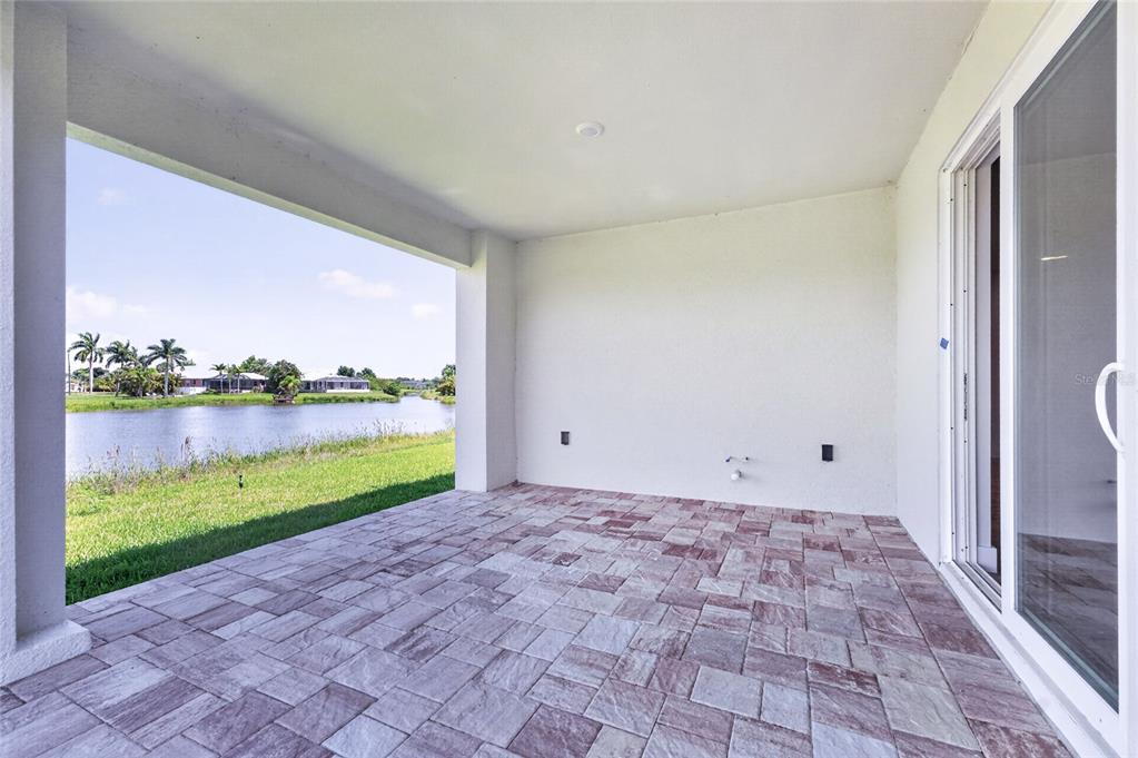A covered patio with paver flooring overlooks a lake and grassy yard — 205 REDWOOD ROAD, ROTONDA WEST, FL