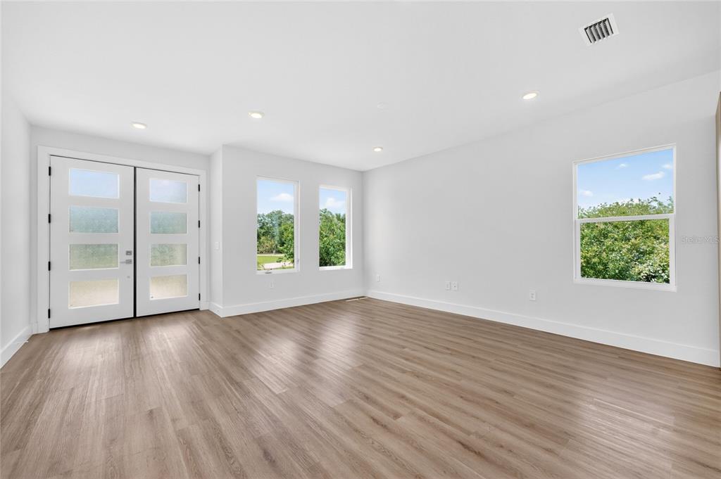 An empty room features light wood-look flooring, white walls, double entry doors, and several windows — 205 REDWOOD ROAD, ROTONDA WEST, FL