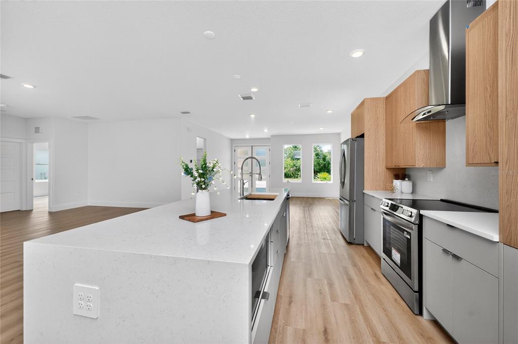 A modern kitchen features a large white quartz island, light wood cabinetry, and stainless steel appliances — 205 REDWOOD ROAD, ROTONDA WEST, FL