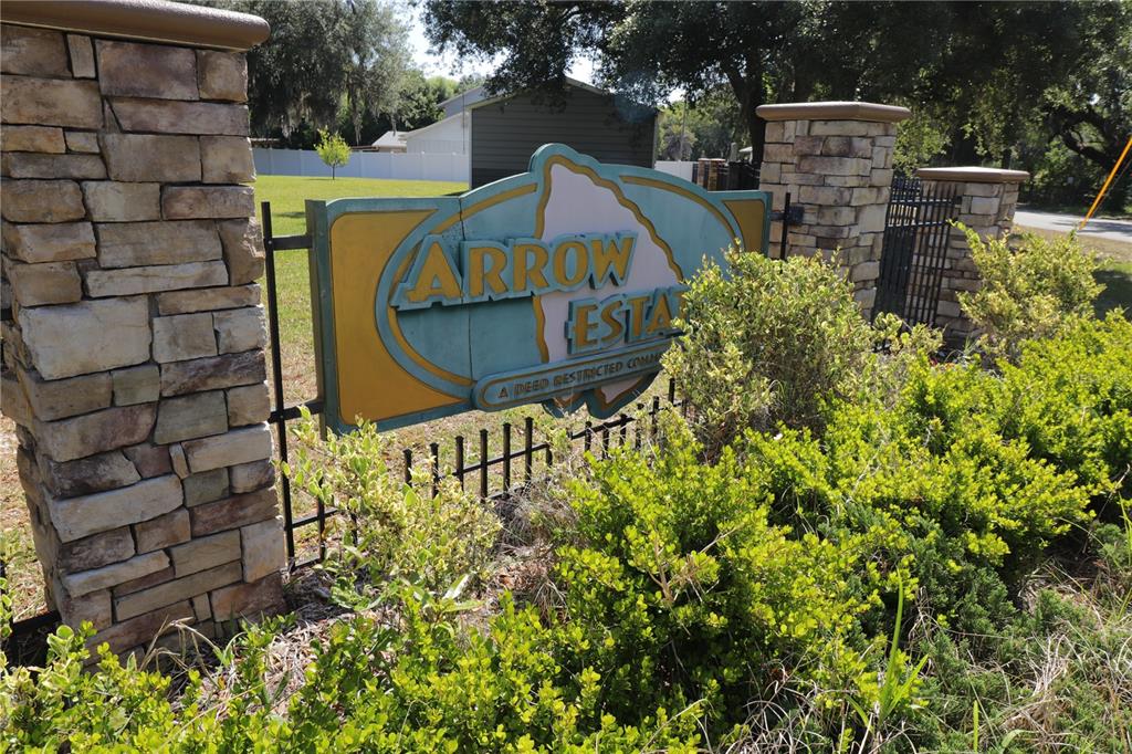 A stone-pillared entrance sign for Arrow Estates stands behind a green hedge — 11470 MAYA COURT, NEW PORT RICHEY, FL