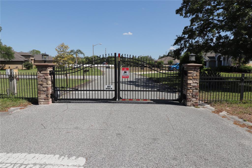 A gated entrance with stone pillars and black metal fencing leads to a residential street — 11470 MAYA COURT, NEW PORT RICHEY, FL