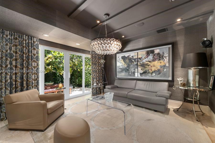 A living room features a crystal chandelier, a gray sofa, and glass doors opening to greenery — 830 E Dilido Dr, Miami Beach FL 33139, MIAMI BEACH, FL