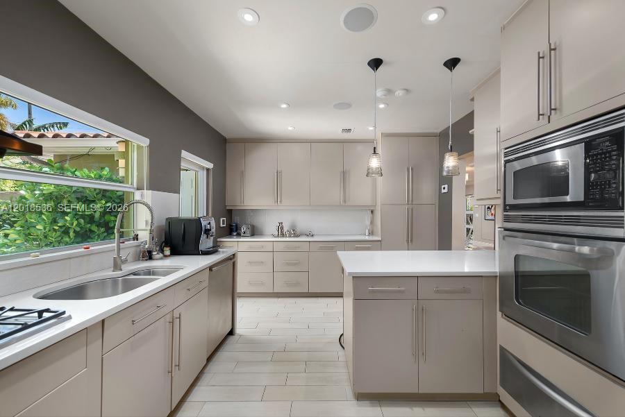 A modern kitchen features light-toned cabinetry, stainless steel appliances, and a window overlooking greenery — 830 E Dilido Dr, Miami Beach FL 33139, MIAMI BEACH, FL