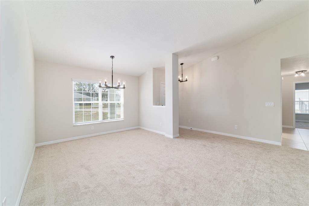 A carpeted dining room features a chandelier, a window with blinds, and a support pillar — 1769 NE 161ST PLACE, CITRA, FL